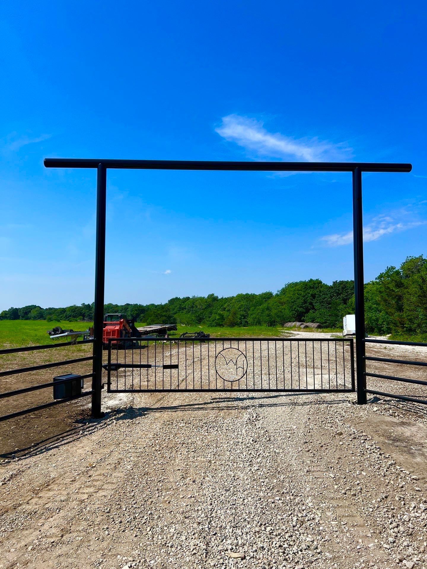 A metal gate is sitting in the middle of a gravel road.