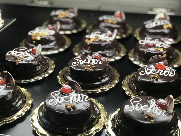 In mostra torte al cioccolato con glassa bianca su cui è scritto "Sochos", guarnite con ciliegie e noci.
