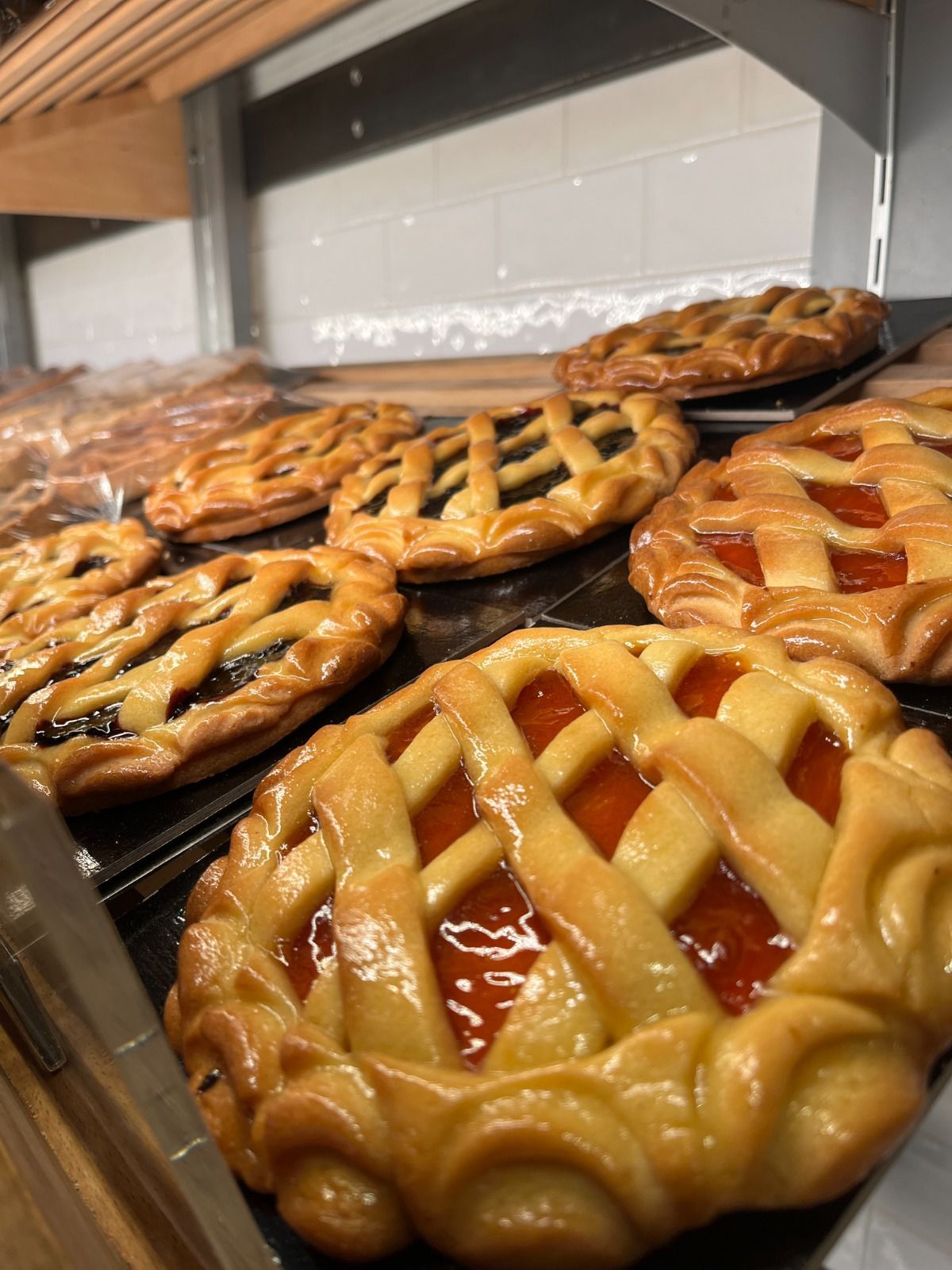 Esposizione di diverse torte di frutta cotte al forno, con la superficie a traliccio, alcune con ripieno scuro, altre con ripieno rosso vivo, in una panetteria.
