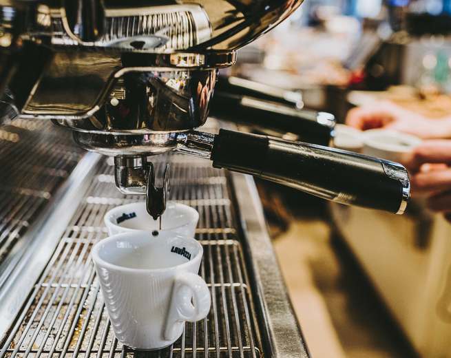 Macchina per caffè espresso che versa il caffè in due tazze bianche su una griglia metallica.
