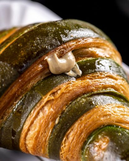 Primo piano di un croissant a strati, a strisce verdi e dorate, farcito con crema chiara.