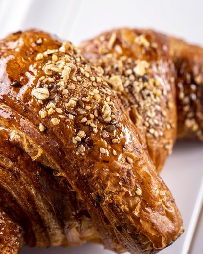 Primo piano di due croissant dorati ricoperti di noci su una superficie bianca.