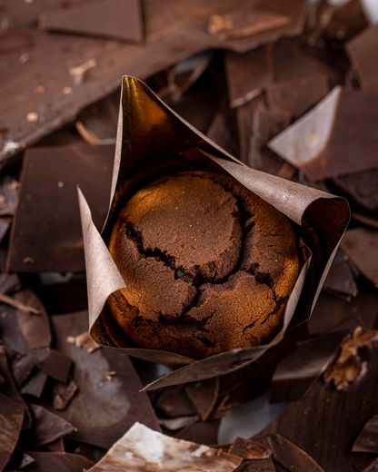 Muffin al cioccolato avvolto in un involucro di carta marrone, circondato da pezzetti di cioccolato.