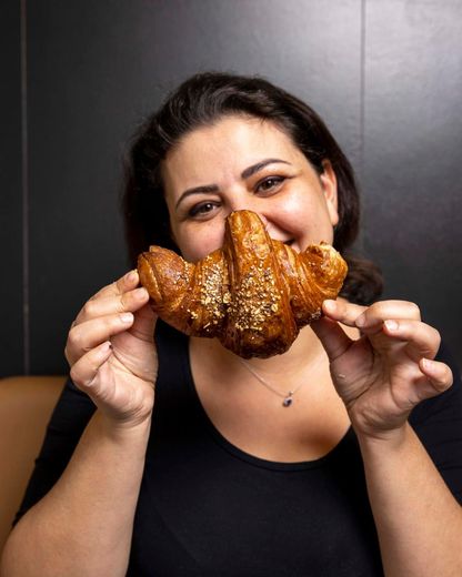 Donna sorridente che tiene in mano un croissant dorato. Top nero, sfondo scuro.