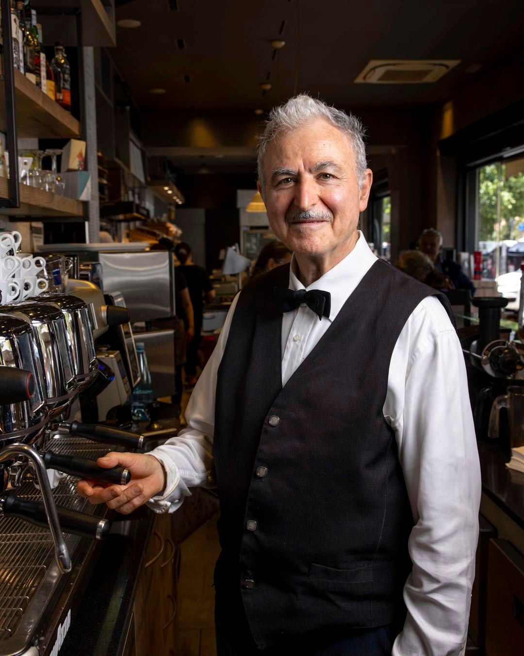 Uomo in gilet e papillon, alla macchinetta del caffè in un bar.
