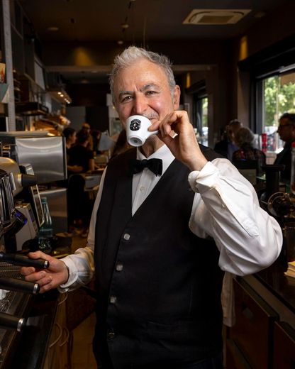 Uomo in gilet e papillon che sorseggia un caffè da una tazza in un bar.
