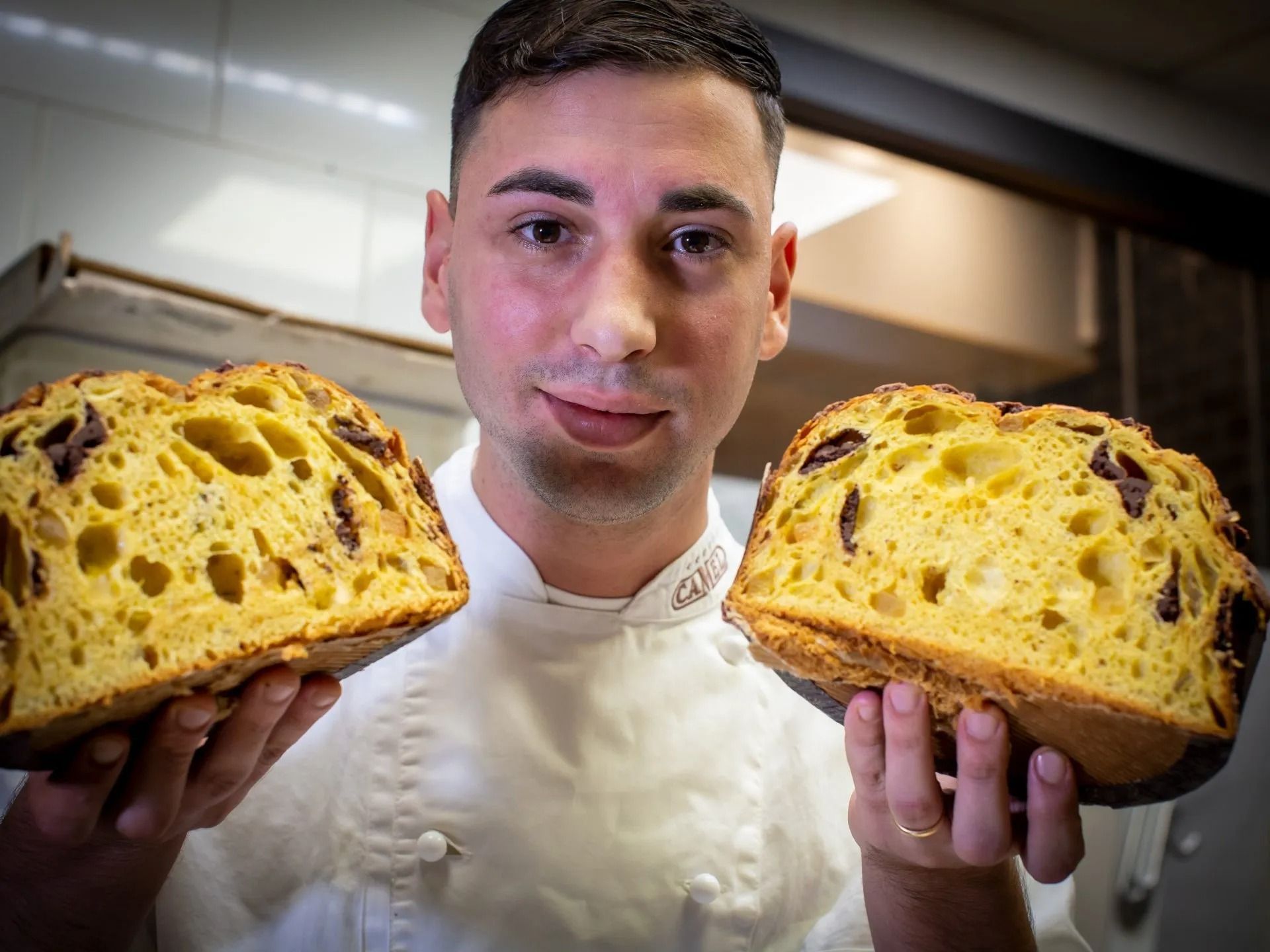 Chef che tiene in mano due metà di una pagnotta dorata e consistente con pezzetti di cioccolato.