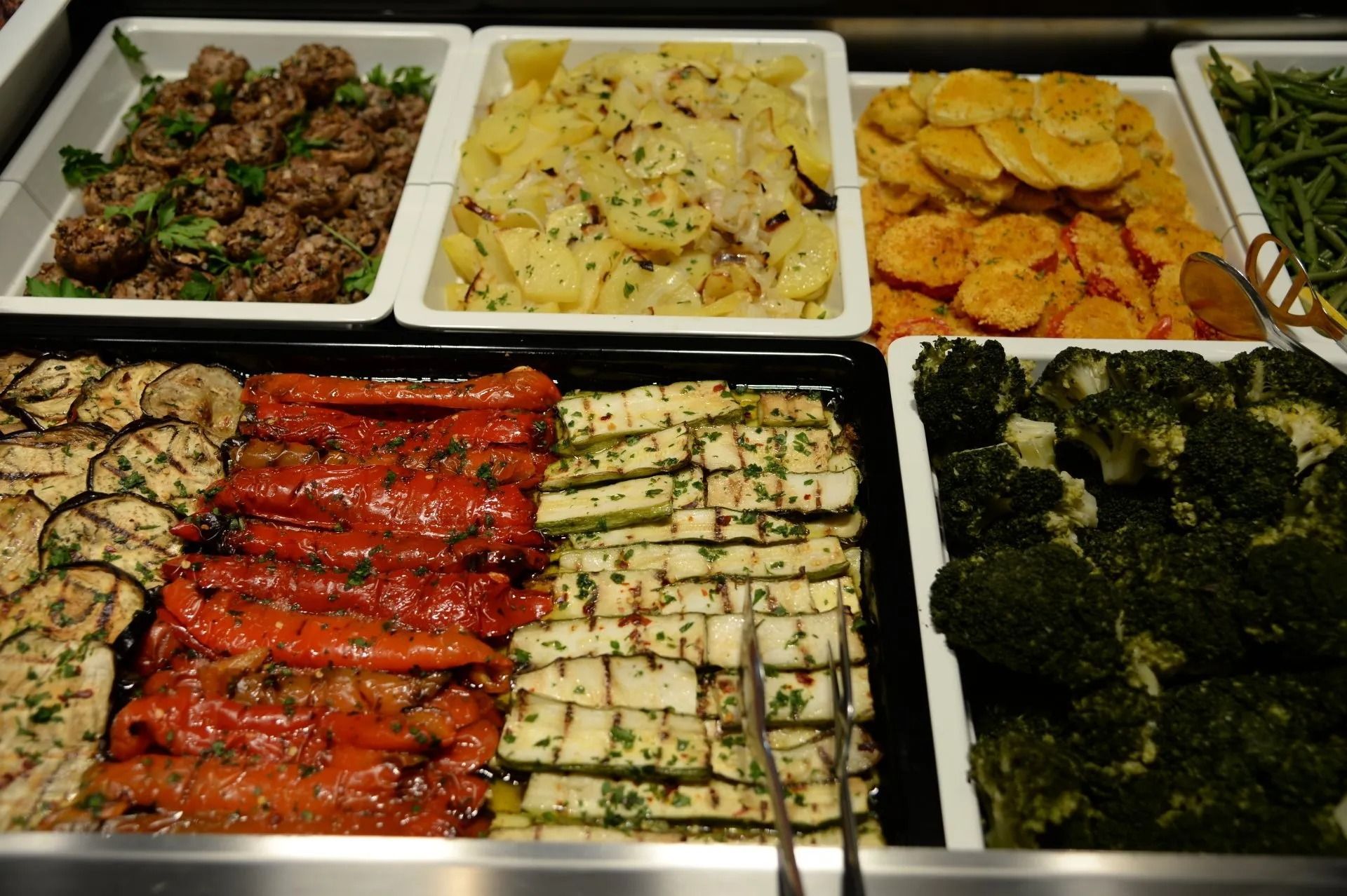 Un buffet con vari contorni e verdure, tra cui patate, peperoni, zucchine e broccoli.