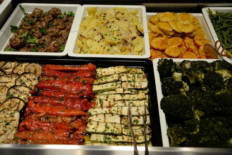 Un buffet con vari contorni e verdure, tra cui patate, peperoni, zucchine e broccoli.