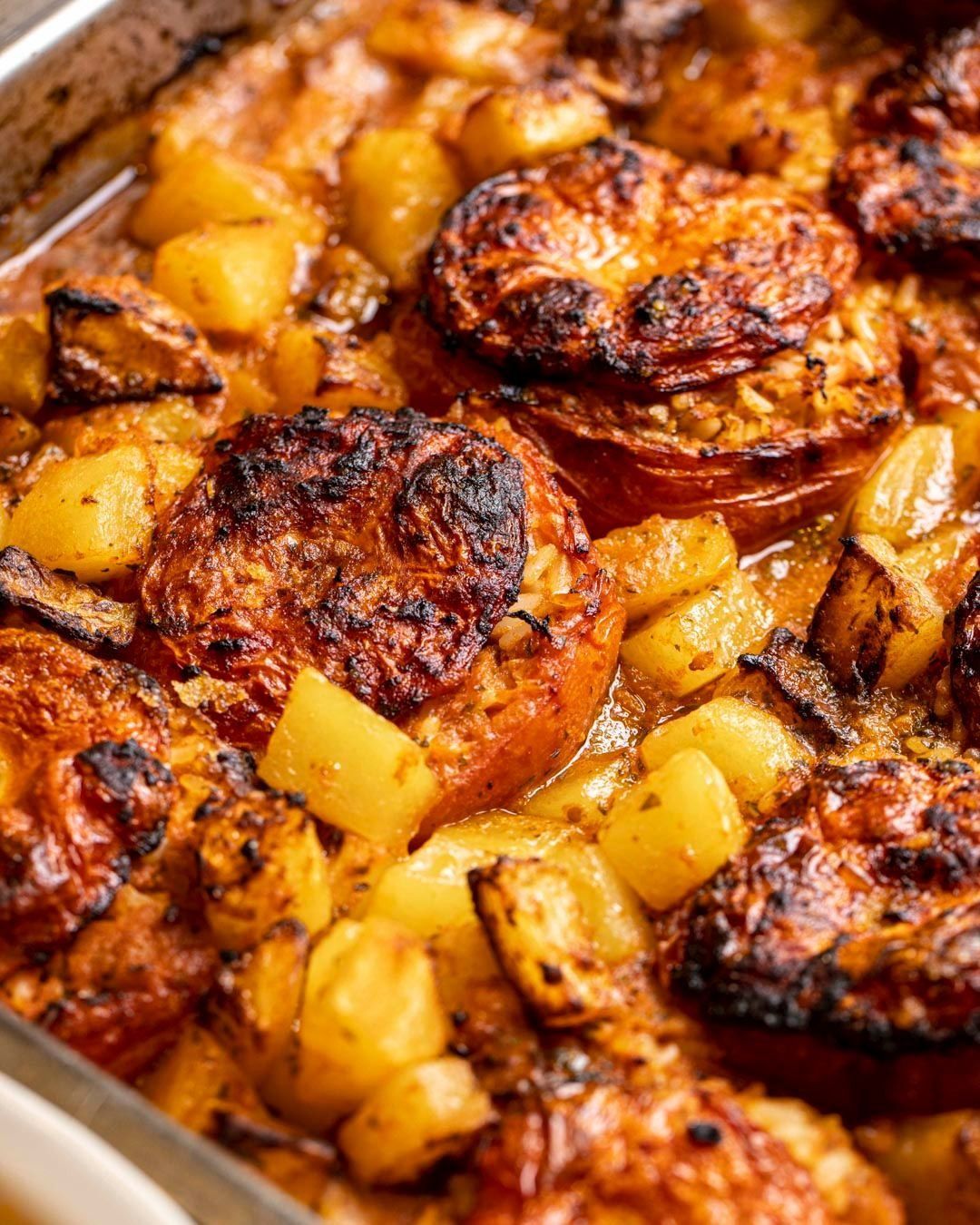 Pomodori e patate arrostiti in una teglia da forno, dorati con erbe aromatiche visibili.