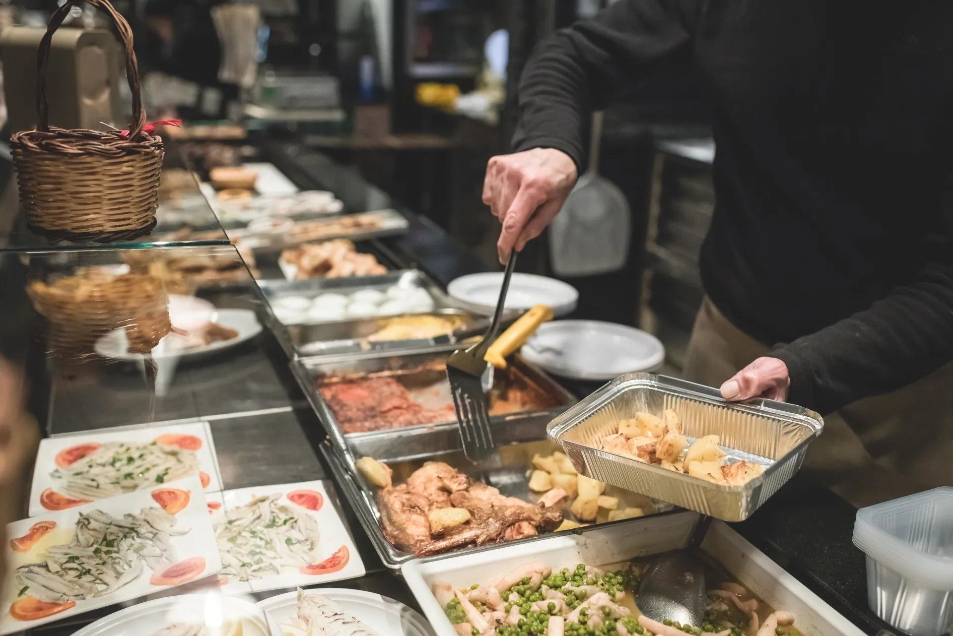 Una persona serve cibo da un buffet. Sono visibili patate, pollo e altri piatti.