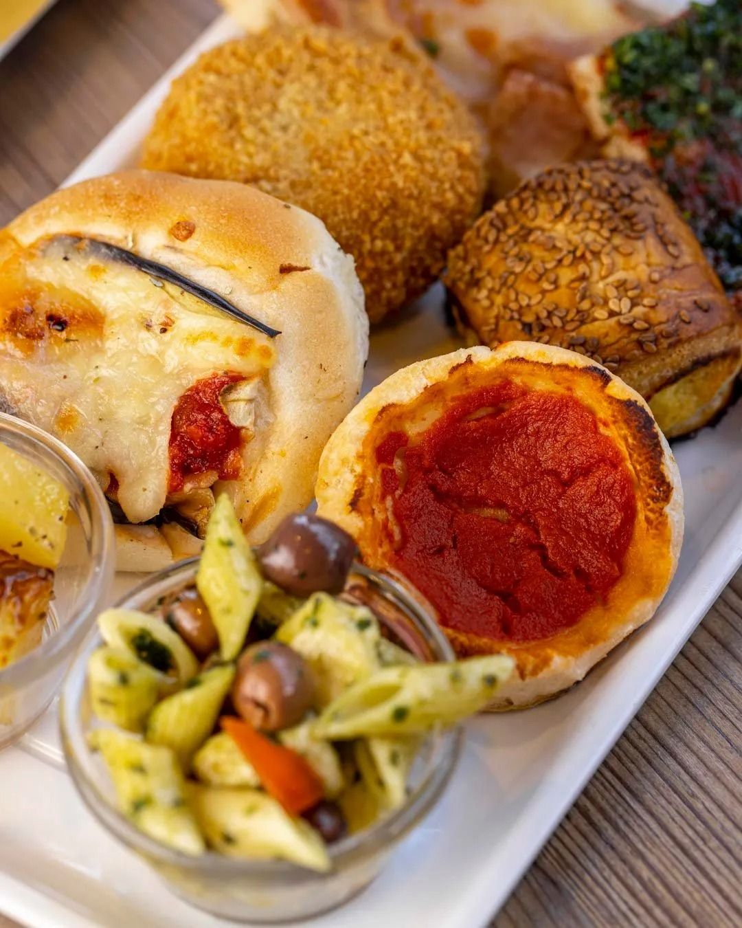 Piatto di antipasti con insalata di pasta, olive, mini pizze e prodotti da forno.