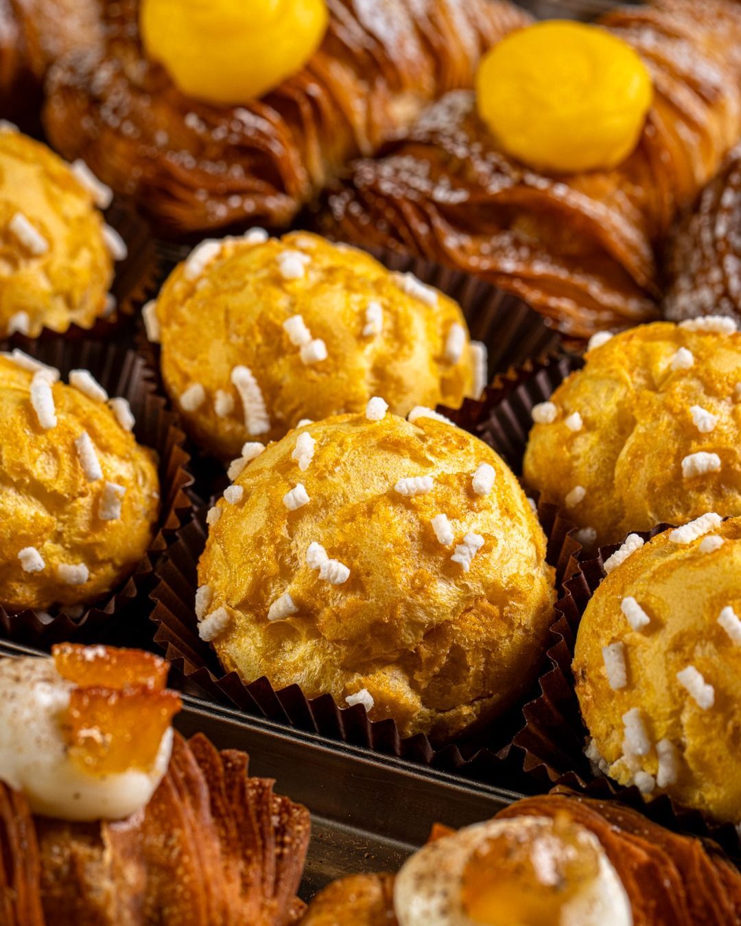 Primo piano di pasticcini assortiti esposti in una vetrina: bignè con granella di zucchero e croissant ripieni.