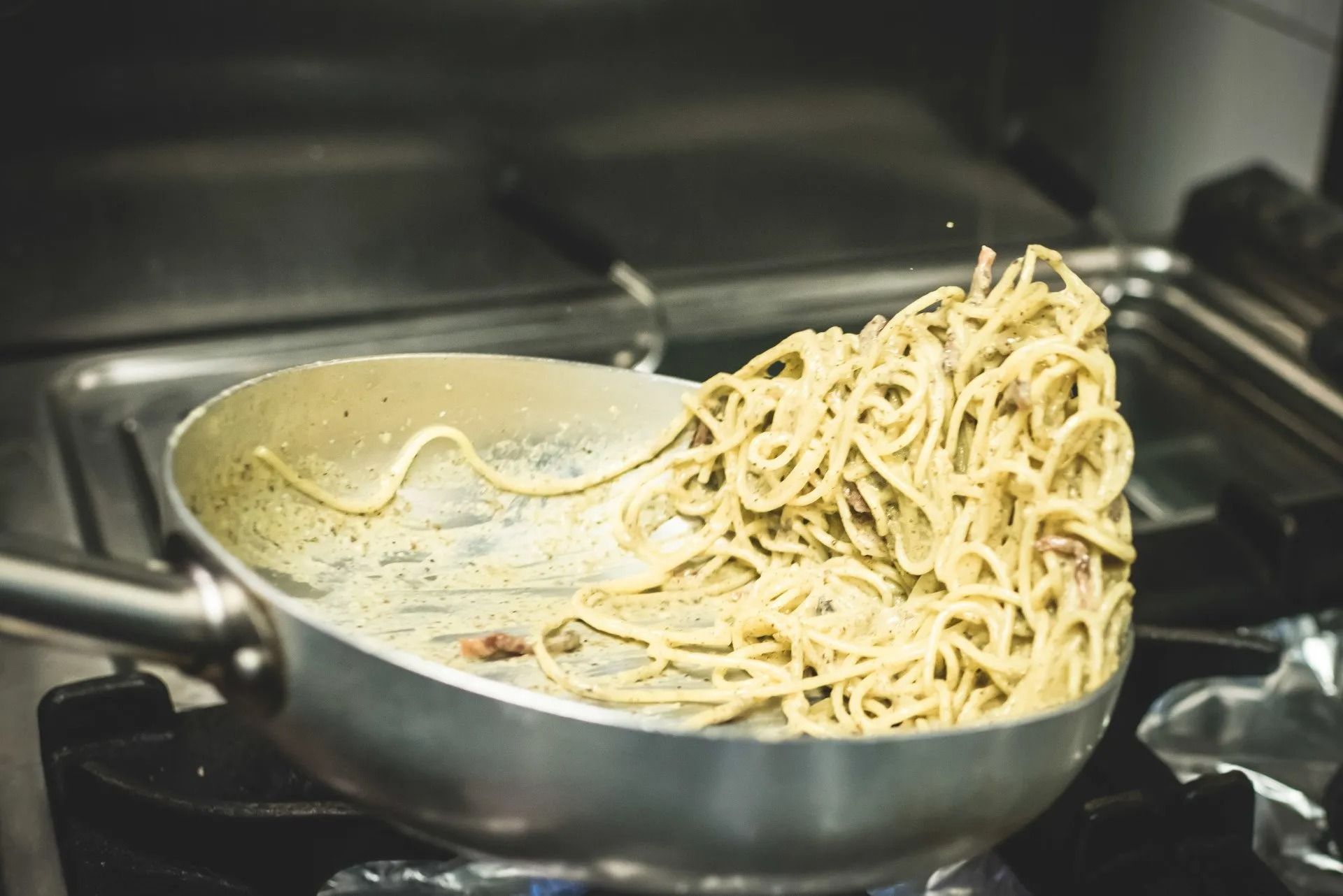 Spaghetti saltati in padella sul fuoco di un fornello a gas.