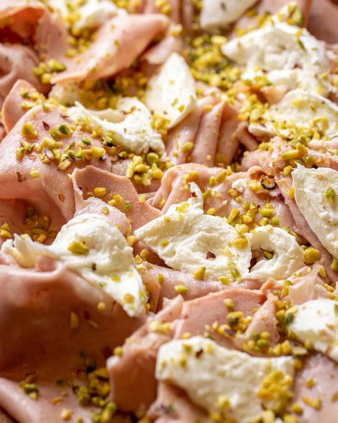 Mortadella tagliata sottile con cucchiaiate di formaggio bianco e una spolverata di pistacchi.