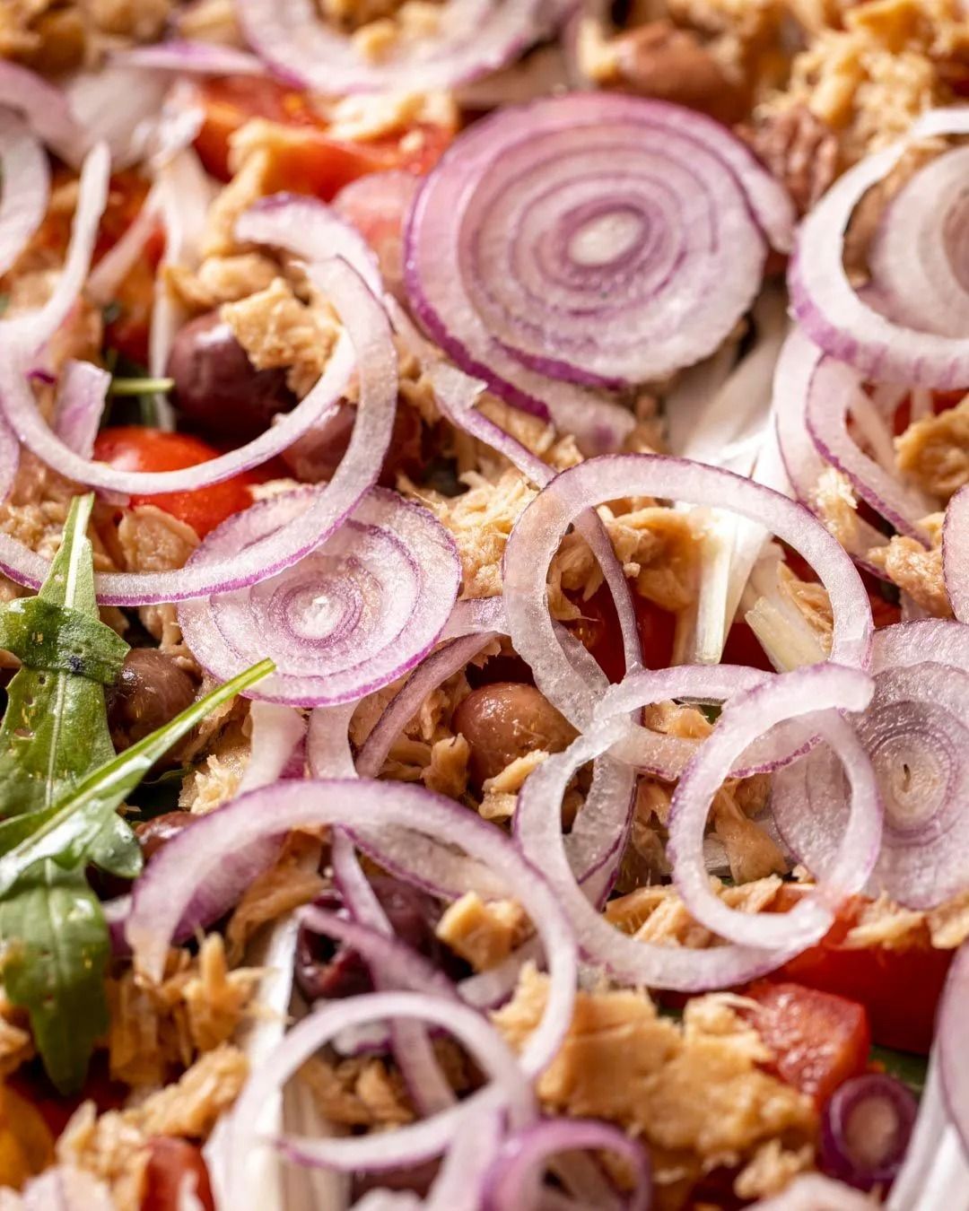 Insalata con tonno, anelli di cipolla rossa, pomodori e rucola.