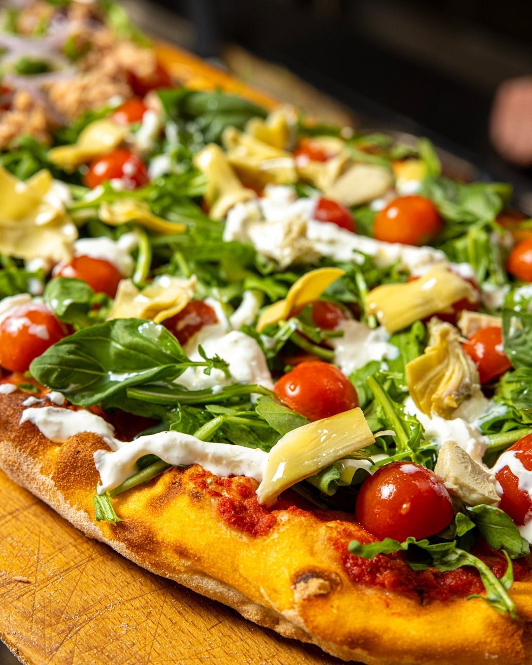 Pizza di pane piatto condita con carciofi, rucola, pomodori e salsa cremosa.