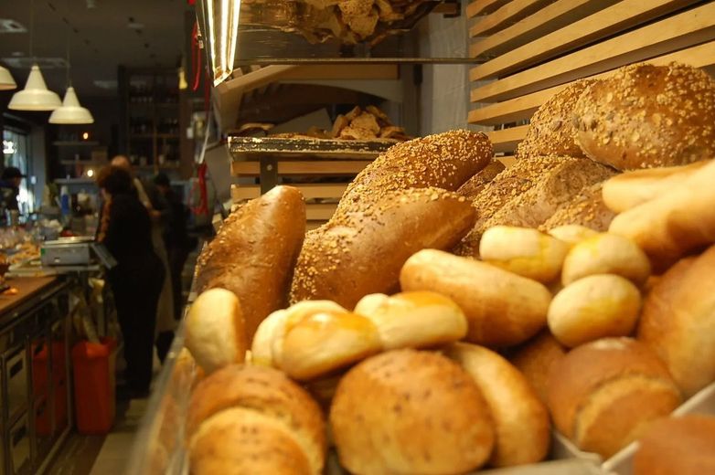 Esposizione di vari tipi di pane, alcuni con semi di sesamo. Sullo sfondo, l'interno del negozio.