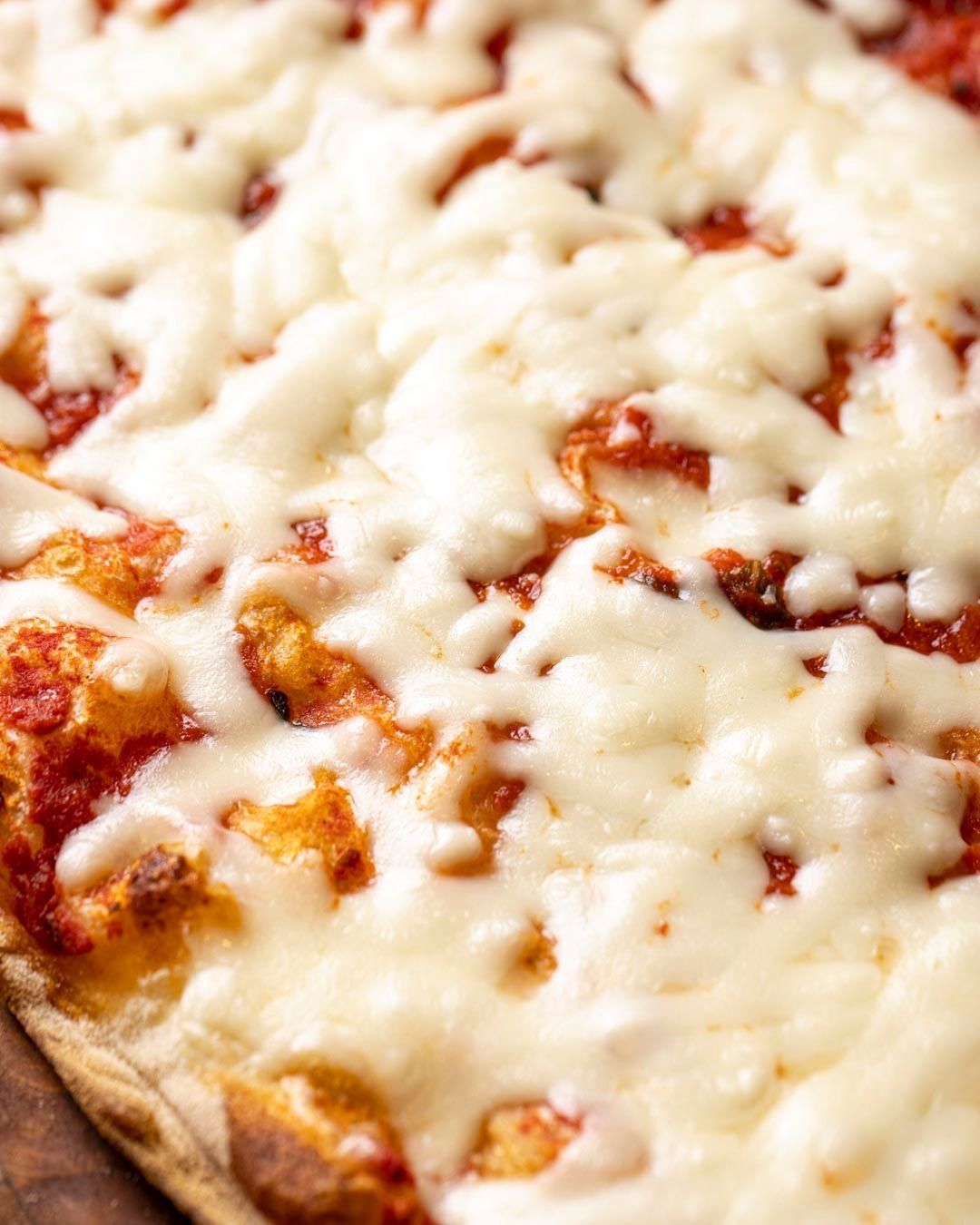 Primo piano di una pizza rettangolare condita con formaggio bianco fuso e salsa rossa visibile.