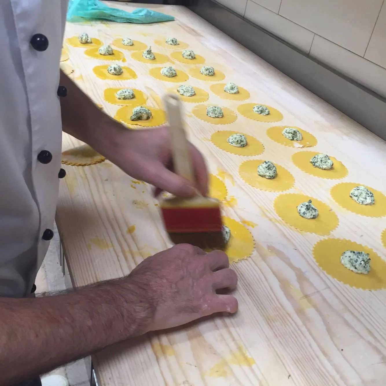Uno chef spennella i cerchi di pasta ripieni di formaggio su un tavolo di legno.