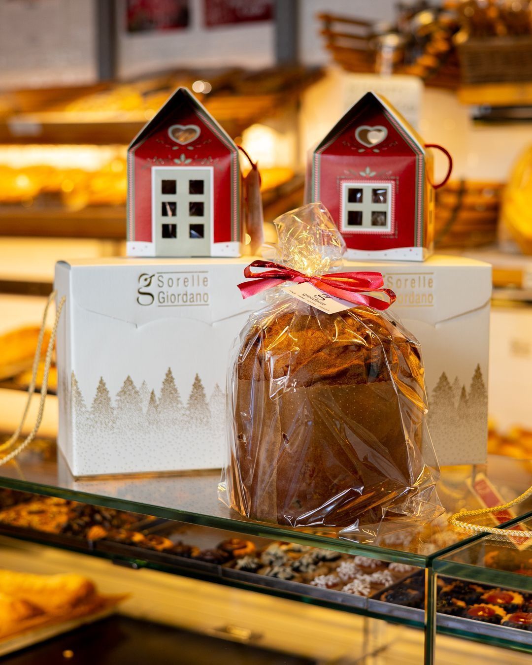 Panettone avvolto in due scatole rosse a forma di casa, esposto in una pasticceria.