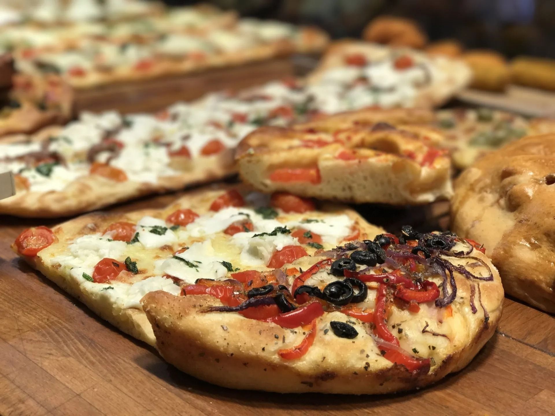 Piadine assortite farcite con verdure, olive e formaggio, disposte su una superficie di legno.