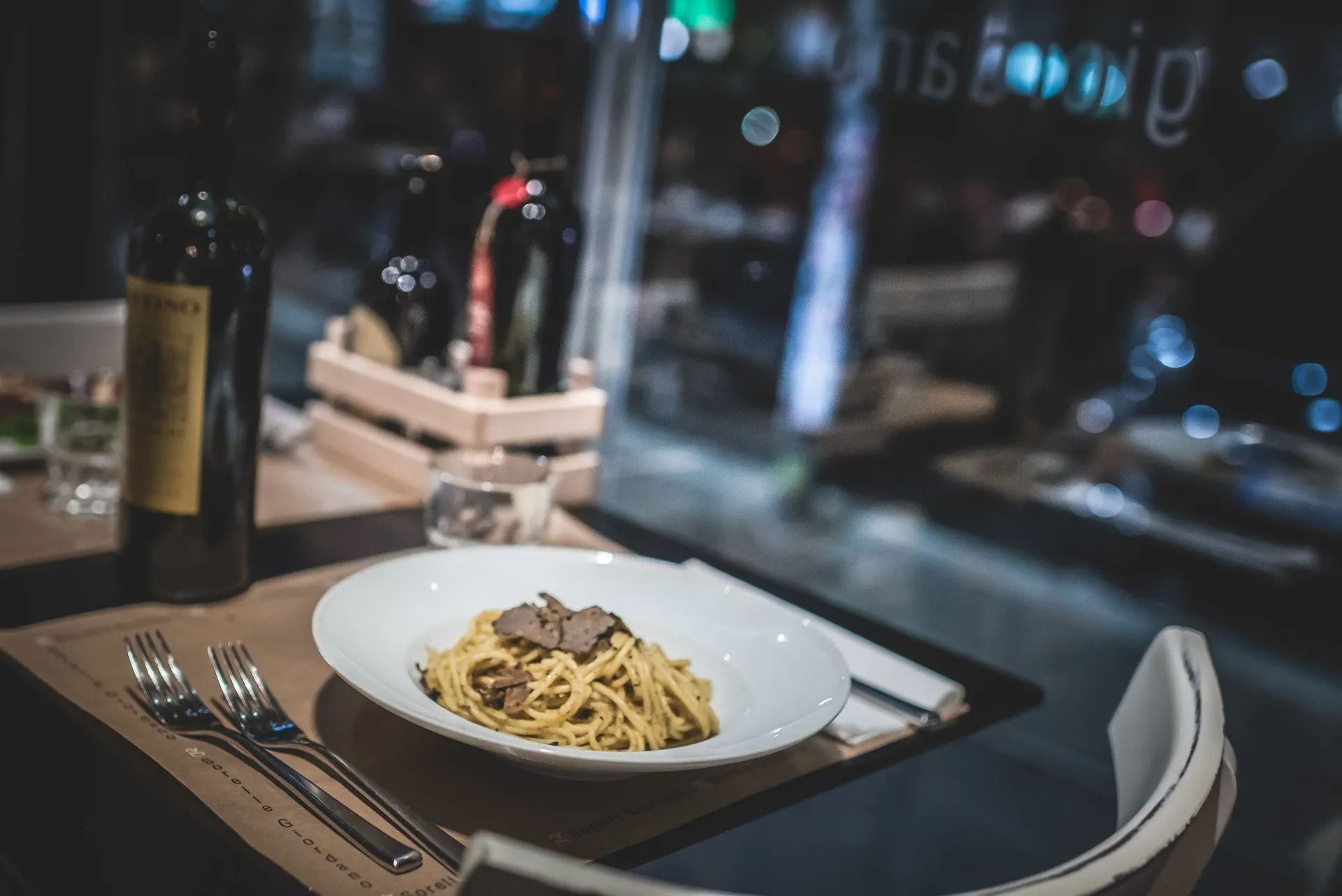 Piatto di spaghetti al tartufo su un tavolo di un ristorante, accanto a bottiglie di vino e posate.