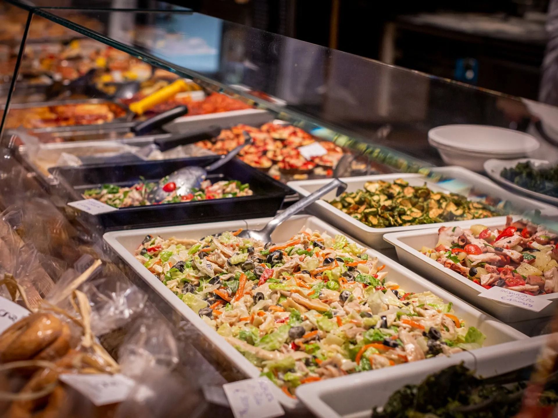 Vetrina buffet con varie insalate e piatti, tra cui frutti di mare, in un ambiente ben illuminato.