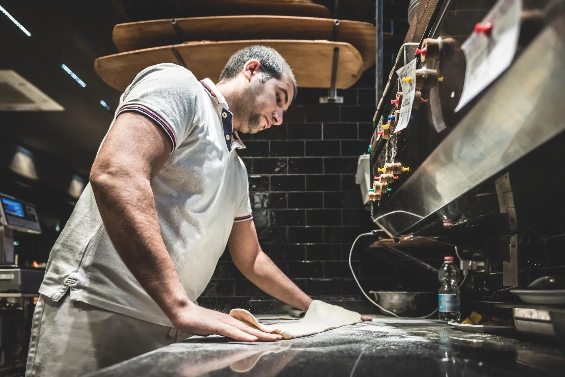 Uno chef con un grembiule bianco modella l'impasto su un bancone in una cucina scarsamente illuminata.