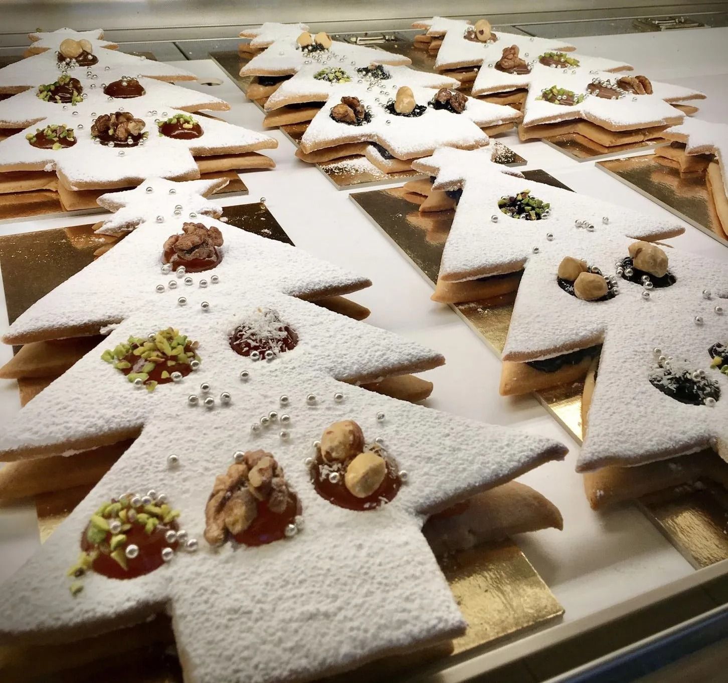 Biscotti a forma di albero di Natale spolverati con zucchero a velo e decorati con noci e granelli.