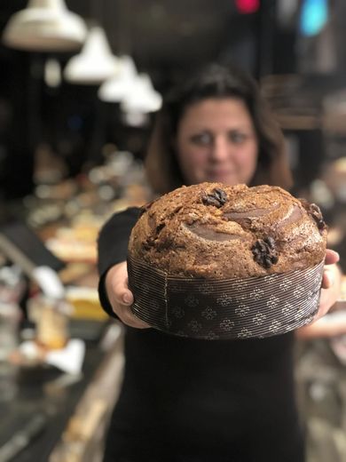 Donna che tiene in mano un grande dolce rotondo di colore scuro. Ambiente interno, panetteria.