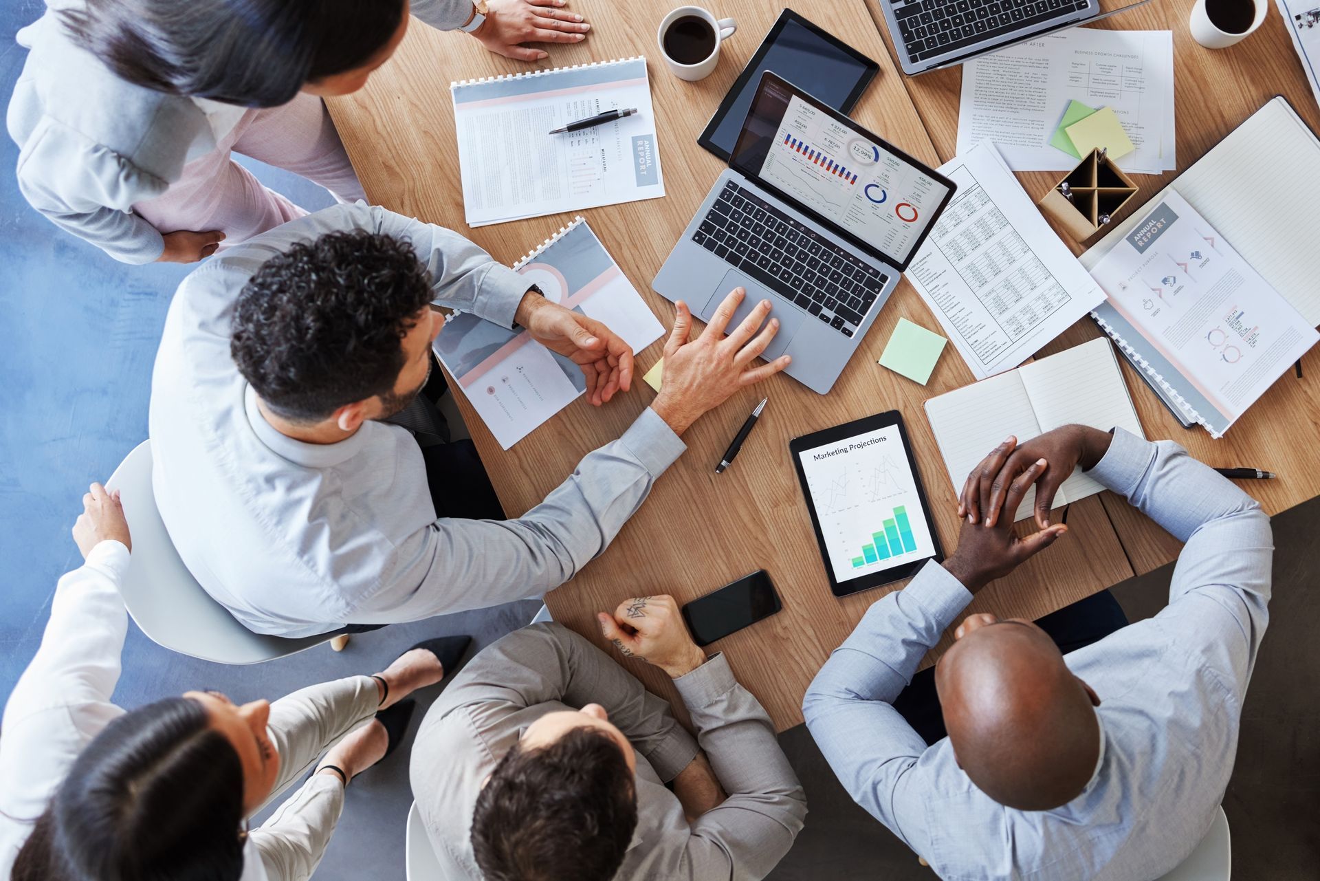An overhead view of a business meeting. 5 staff in suite overlook one laptop