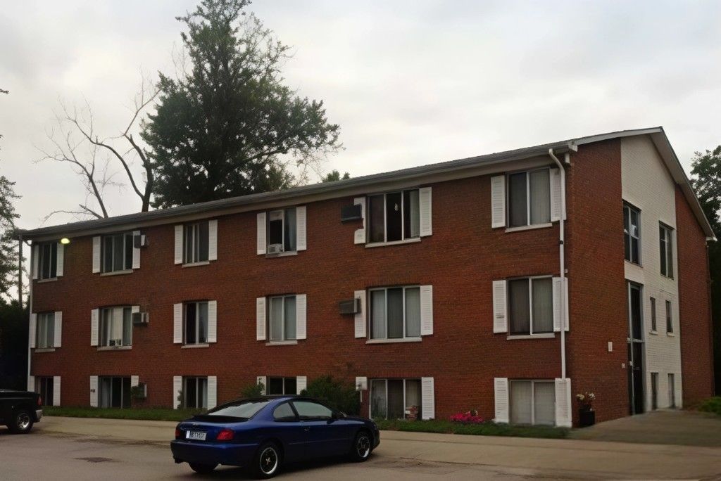 A blue car is parked in front of a large brick building