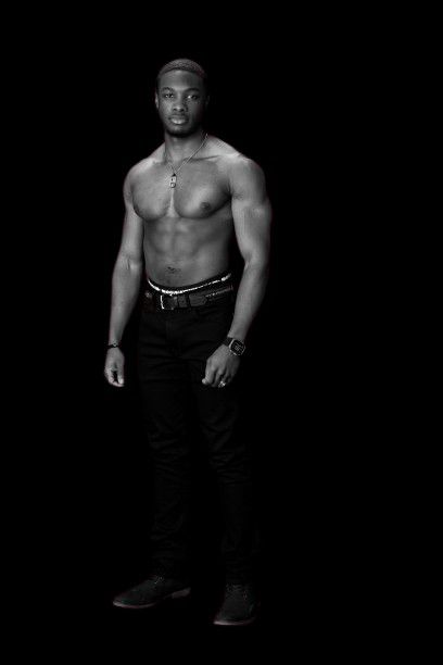 a black and white photo of a shirtless man standing in front of a black background .