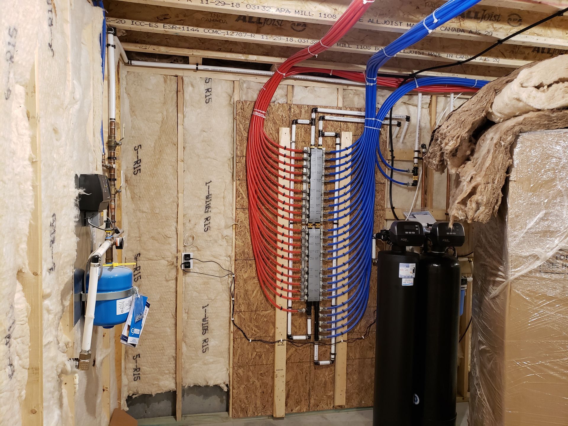 Plumbing system in a basement. Red and blue pipes connected to a manifold, with a black tank and water meter.