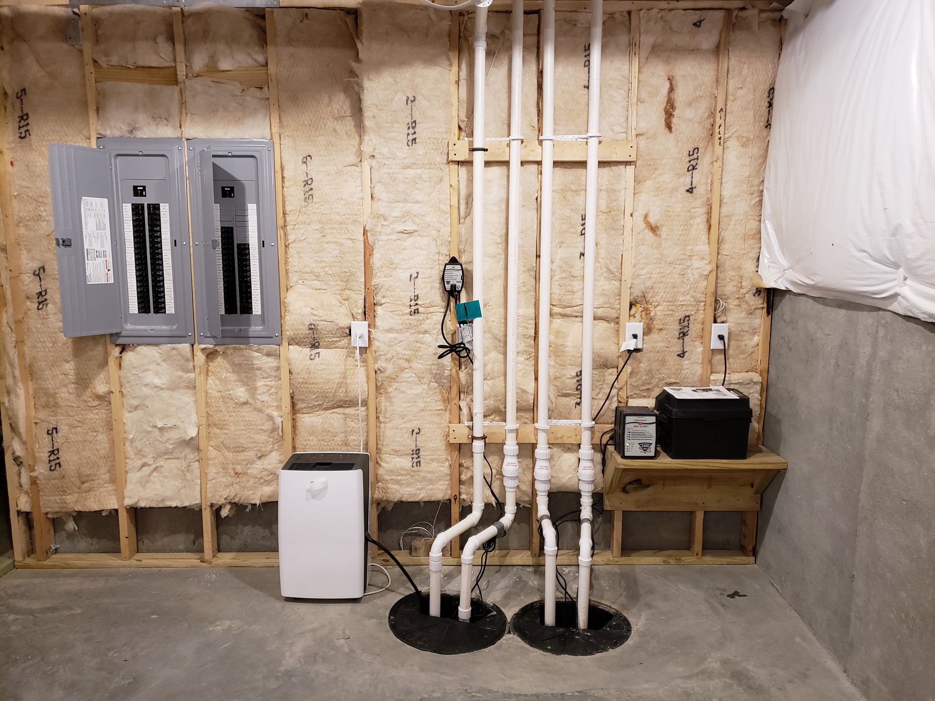 Basement interior with electrical panel, sump pumps, and a dehumidifier against unfinished walls.