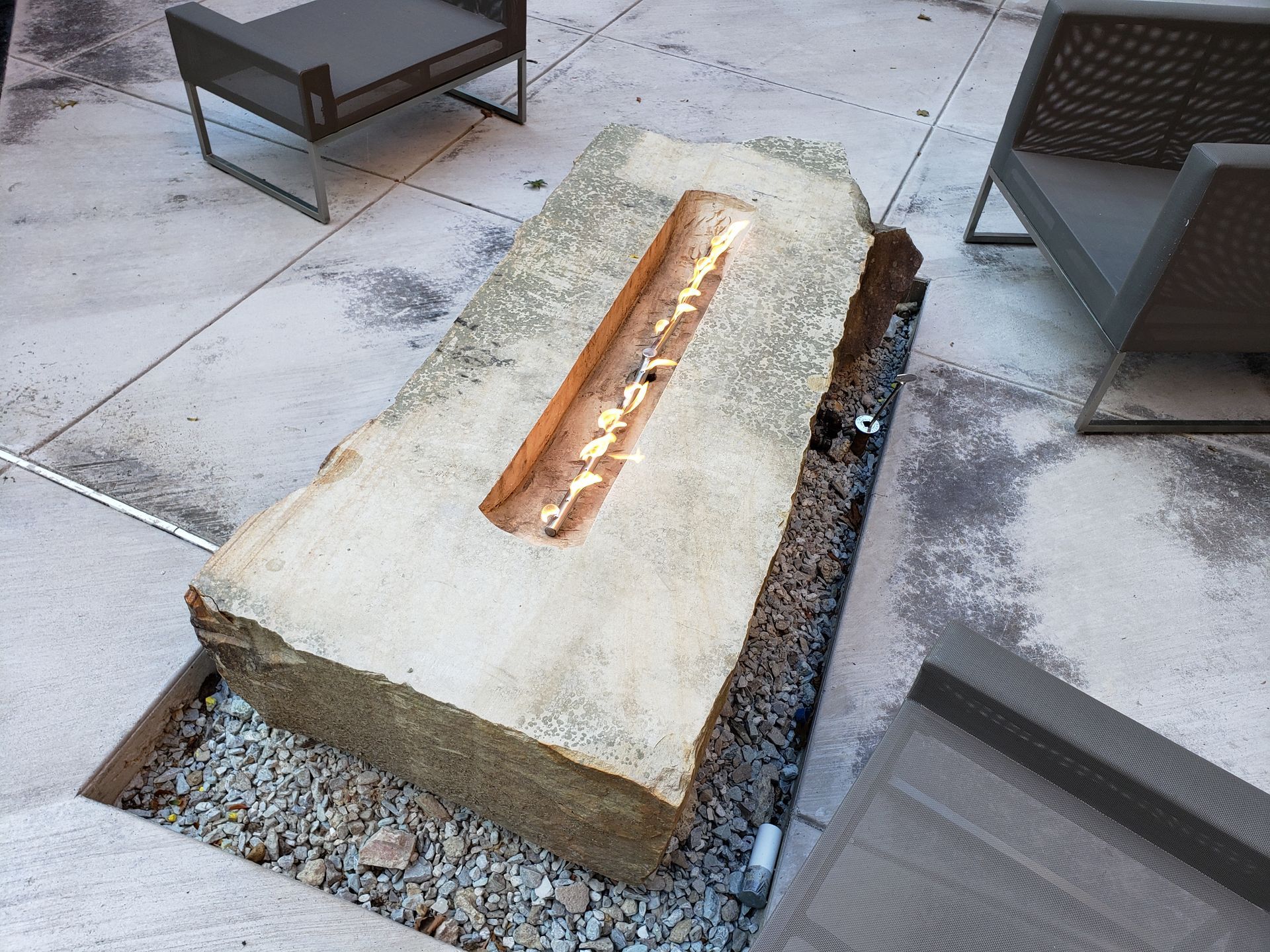 Stone water feature with a long, narrow trough, set in gravel and concrete.