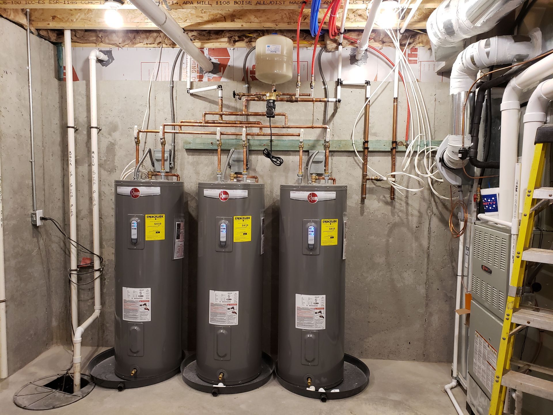 Three water heaters in a basement, with copper pipes and plumbing.