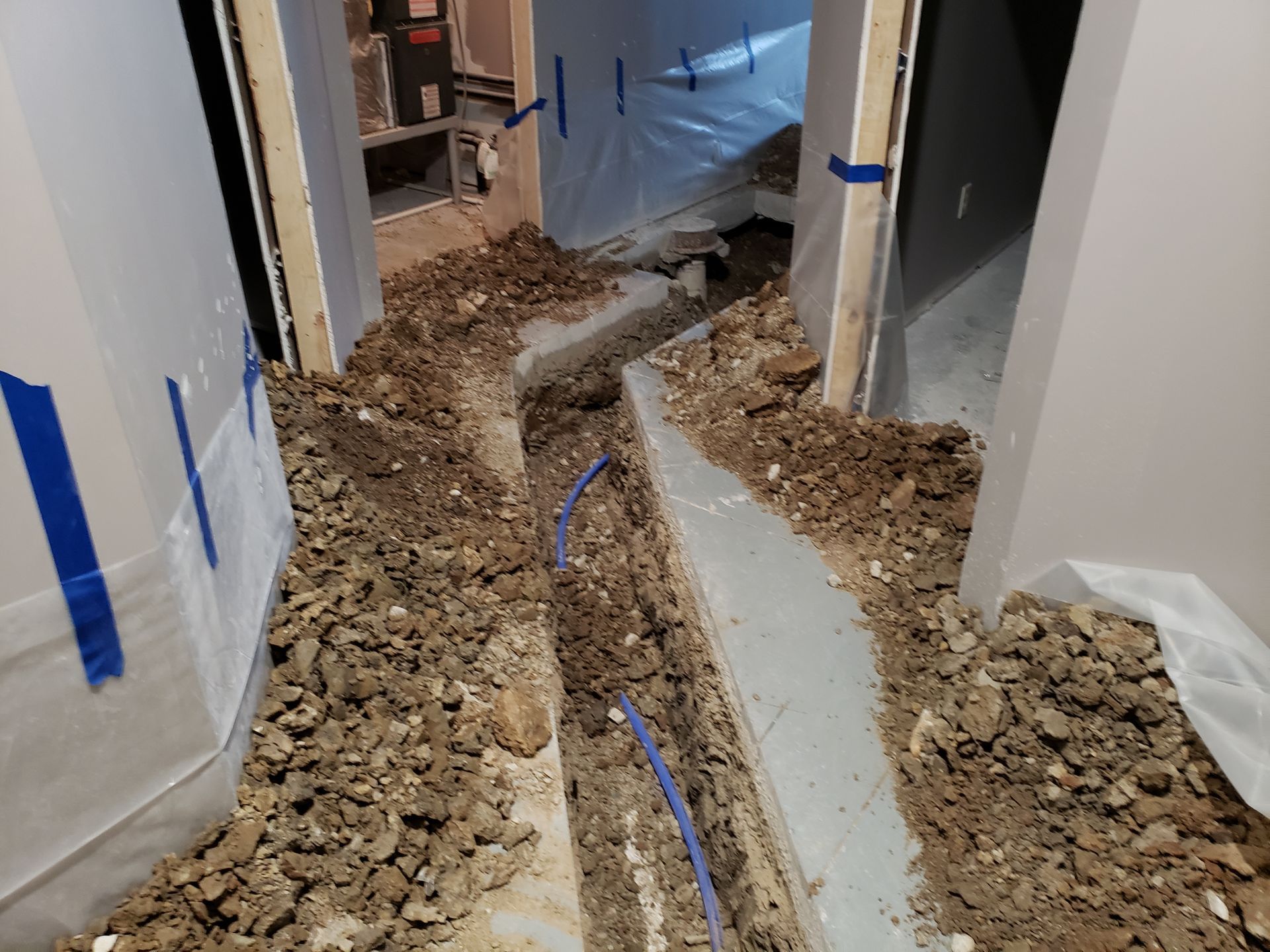 A dirt-filled trench with blue pipes runs through an unfinished interior doorway.