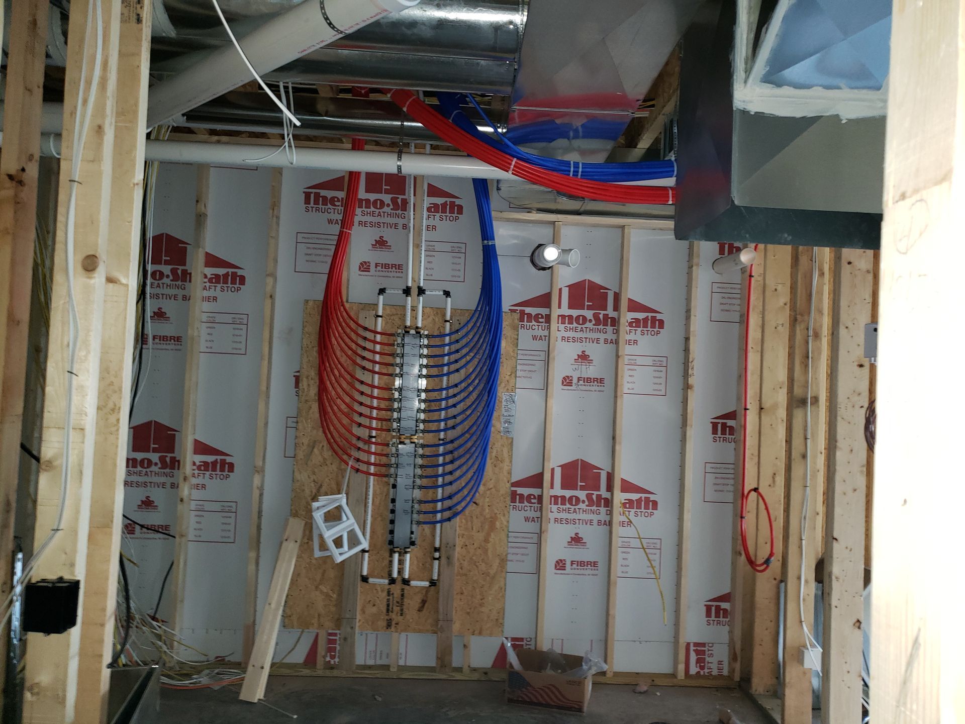 Interior view of a construction site. Red and blue PEX tubing installed on a wall. Ductwork and framing visible.