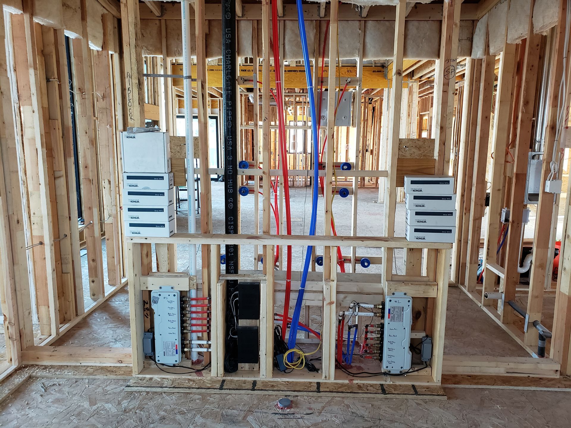 Interior view of a wooden framed wall with installed plumbing pipes and electrical boxes.
