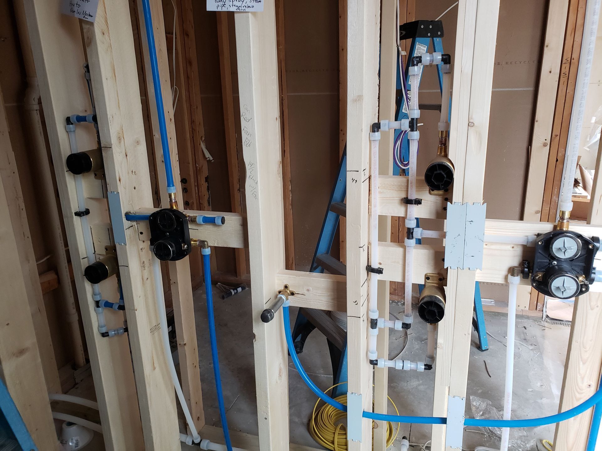 Framing of a wall with blue plumbing and black valve boxes installed.