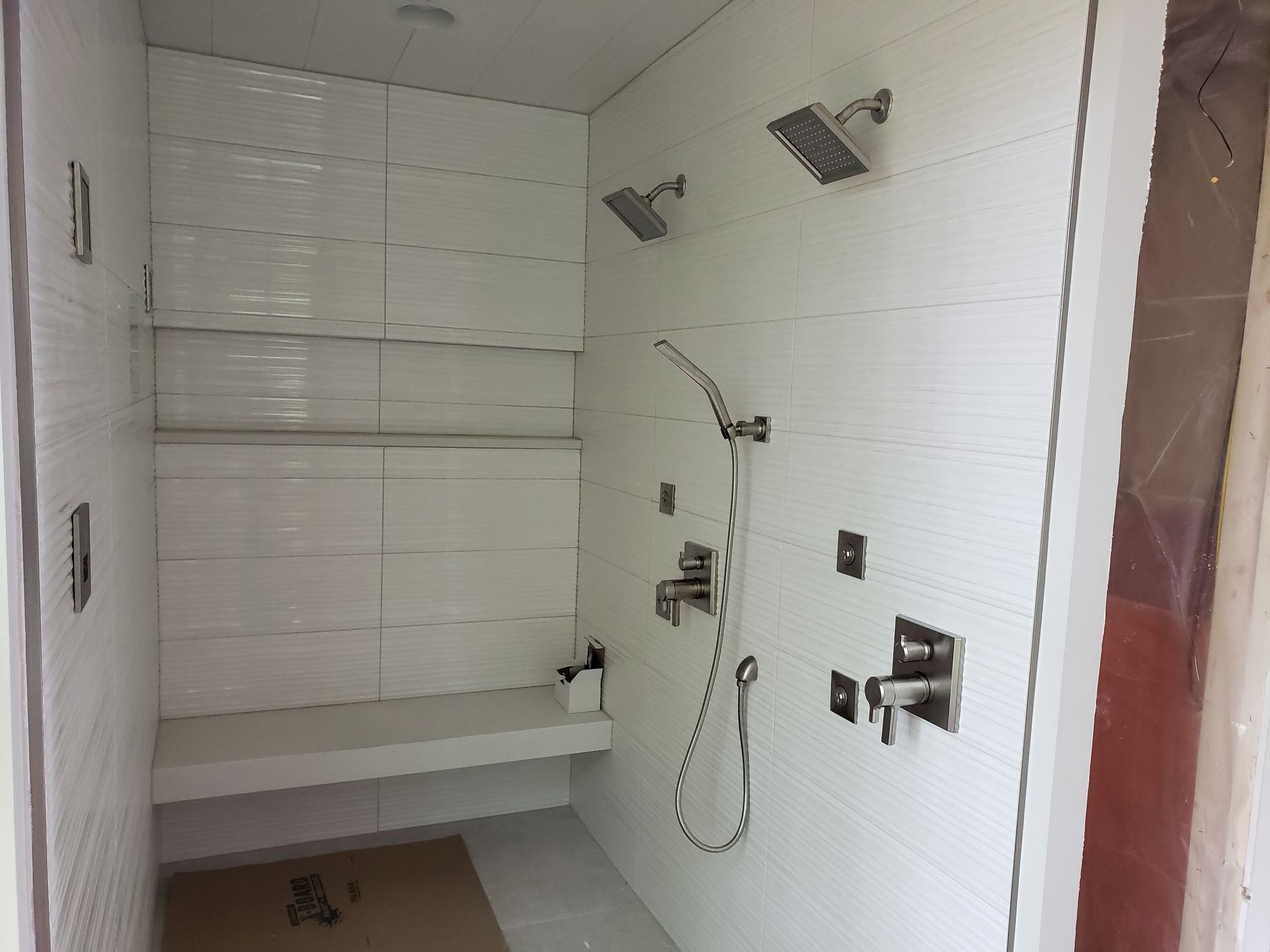 White tiled shower with built-in bench, shelves, and multiple showerheads and fixtures.