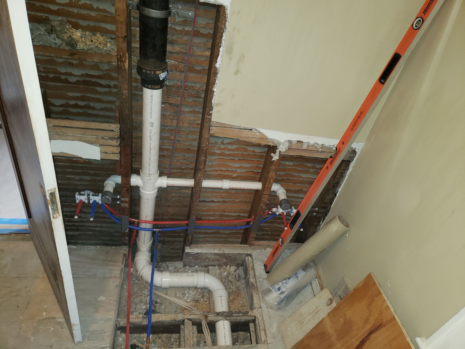 Plumbing pipes exposed in a wall and floor during a bathroom renovation, showing drain, water supply, and leveling tool.
