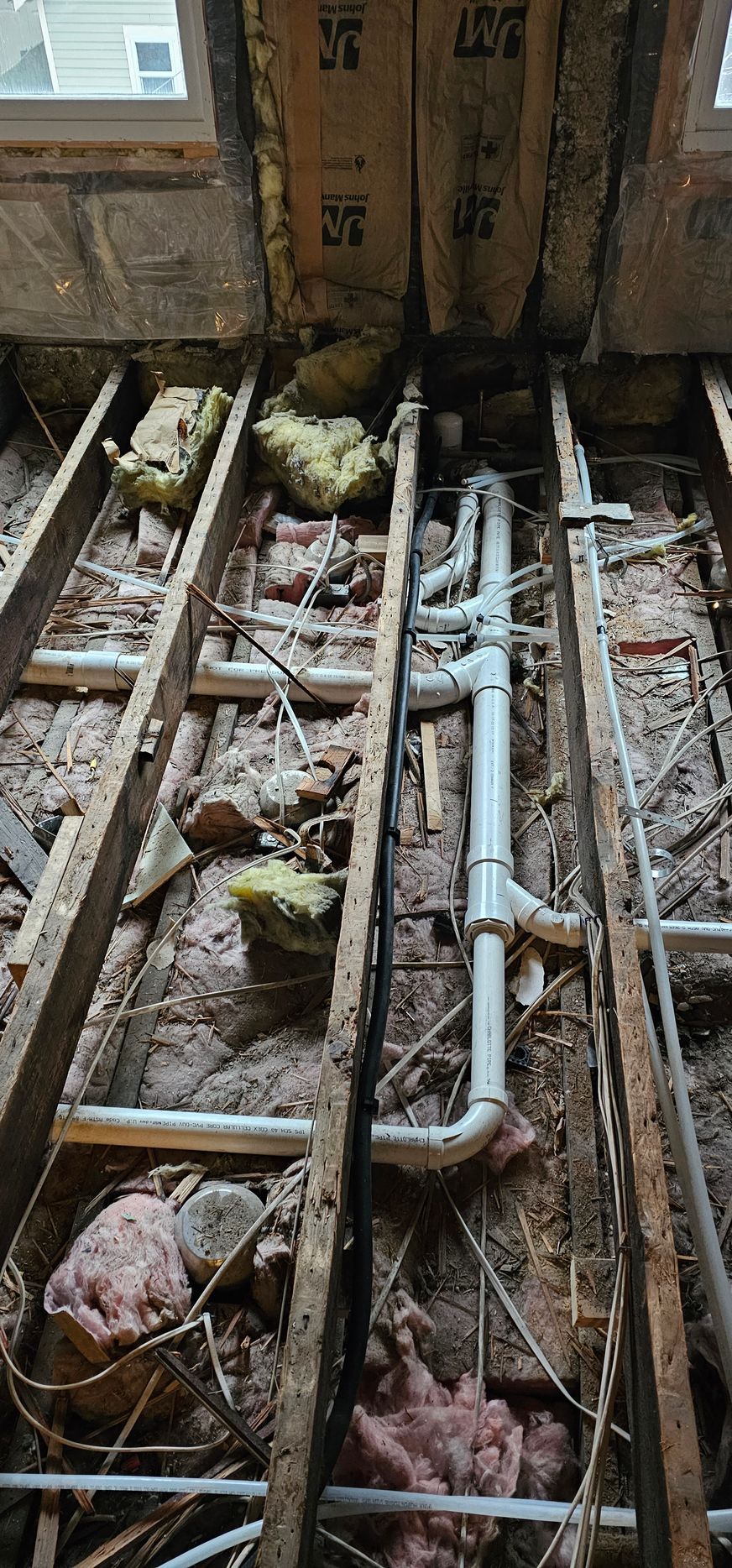 Plumbing and insulation exposed between wooden joists in a construction setting.