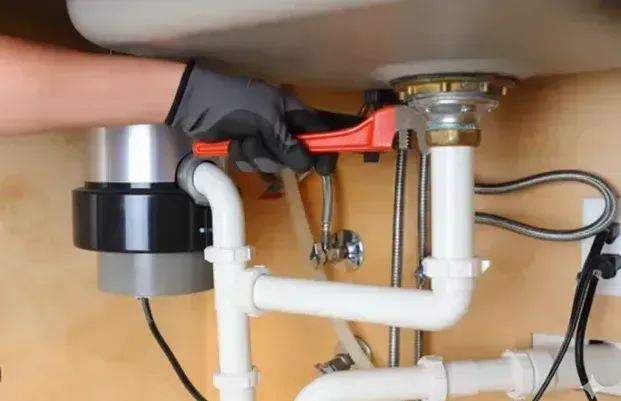 Person using a wrench to tighten a pipe under a sink; interior setting.