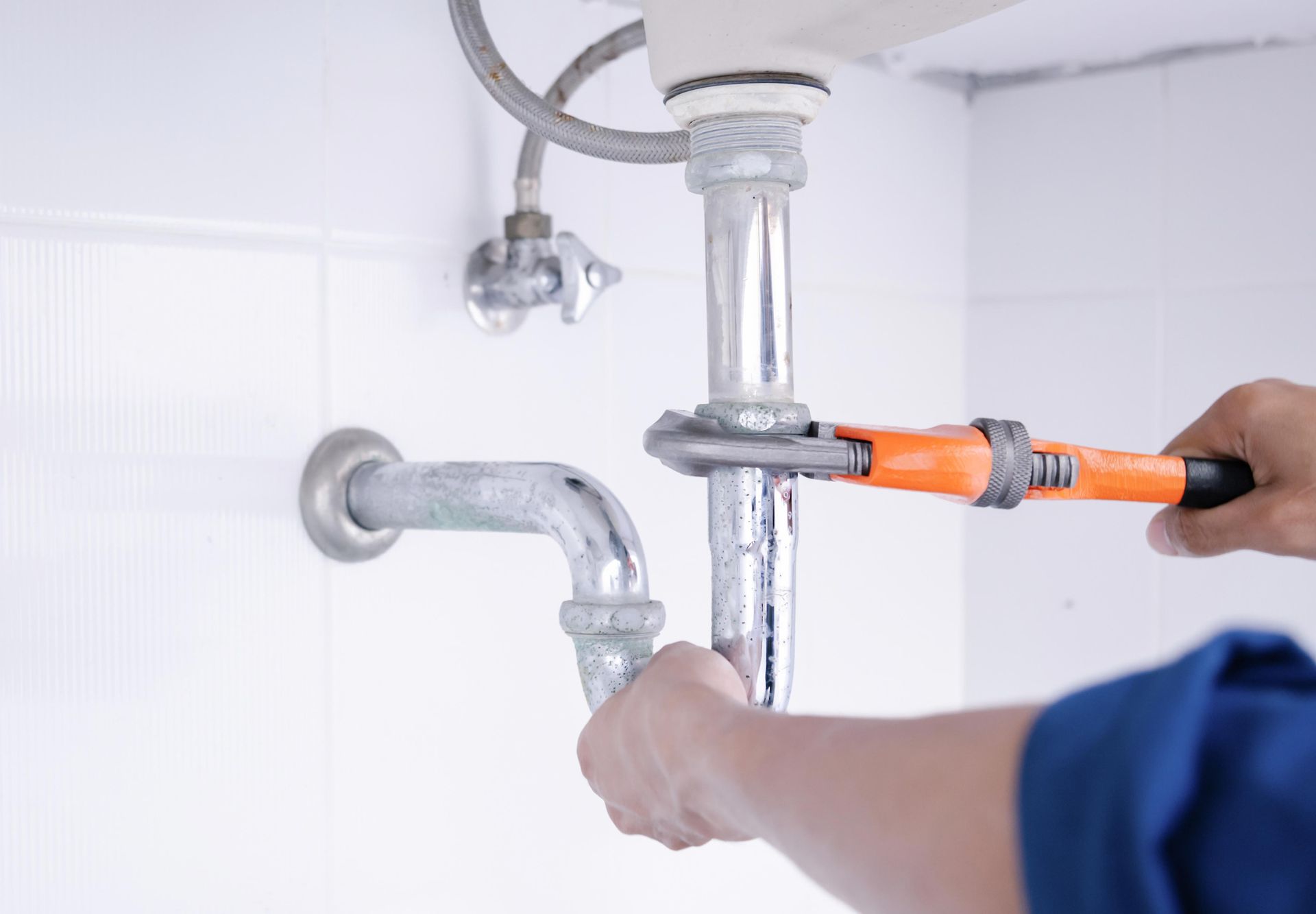 Plumber working in the bathroom repairing leaking sinks with adjustable wrench.