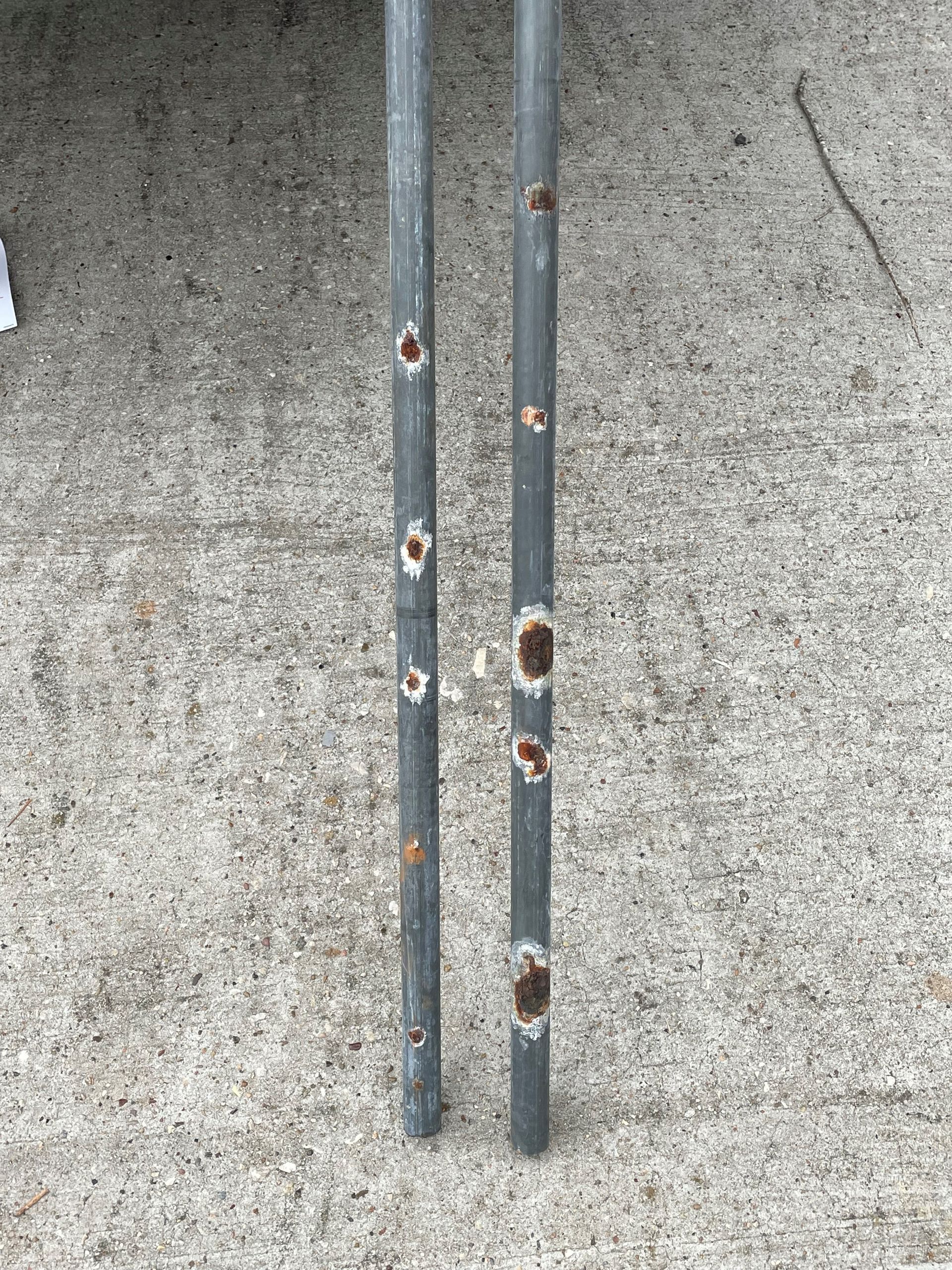 Two metal poles with holes in them are sitting on a concrete surface.