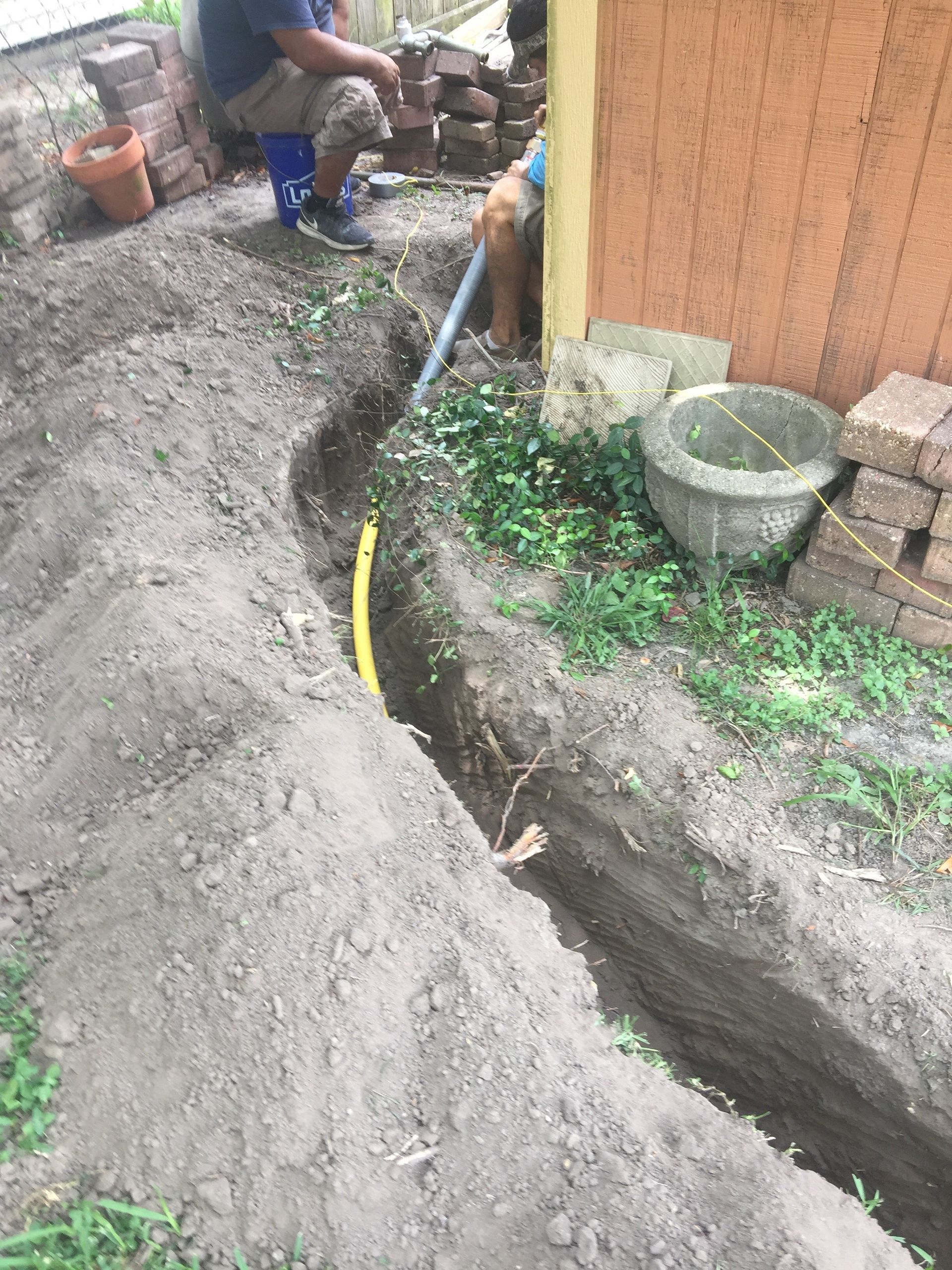 A man is kneeling in the dirt next to a hose.