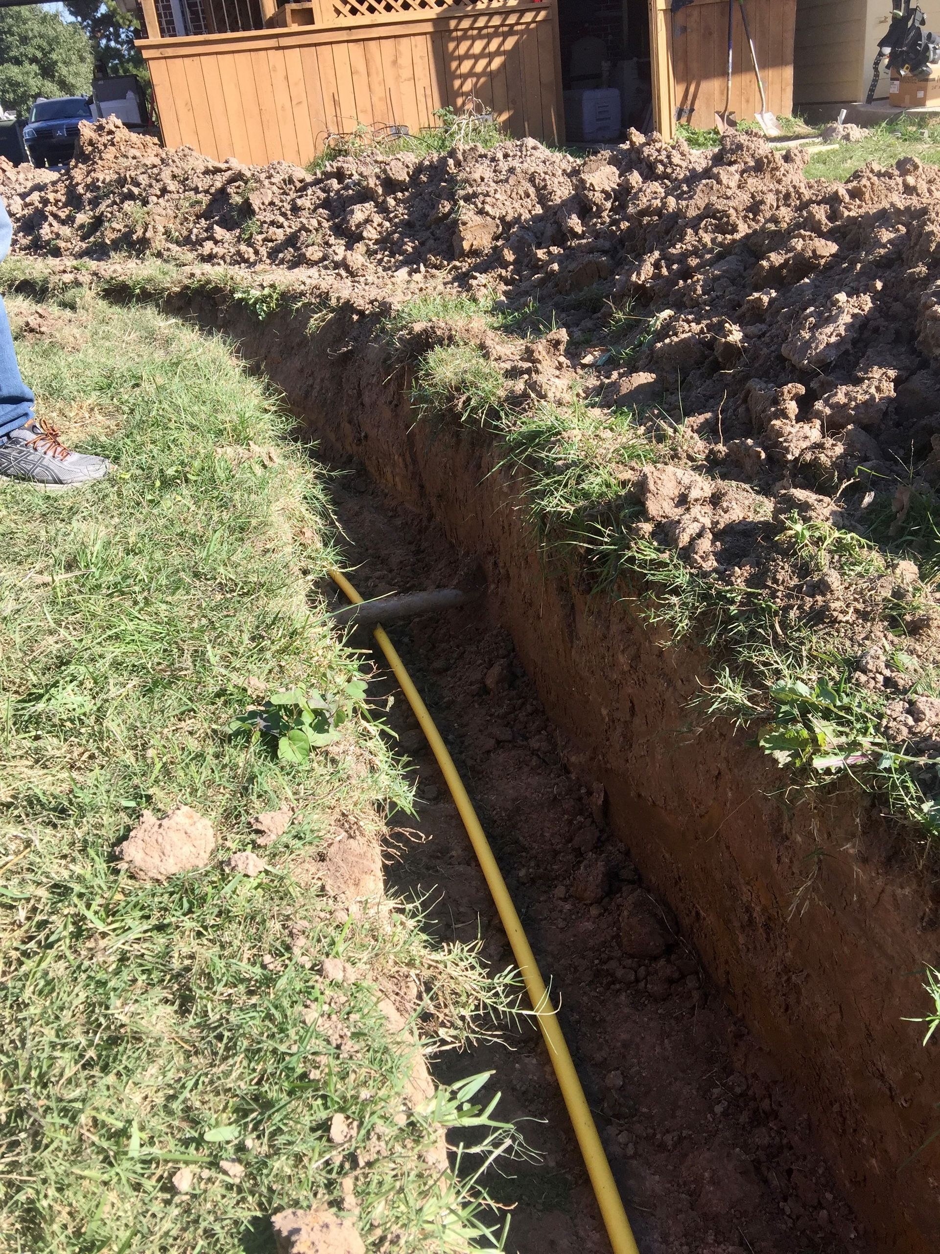 A person is digging a hole in the ground with a yellow hose.